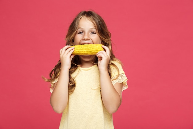 Menina bonita jovem comendo milho na parede rosa