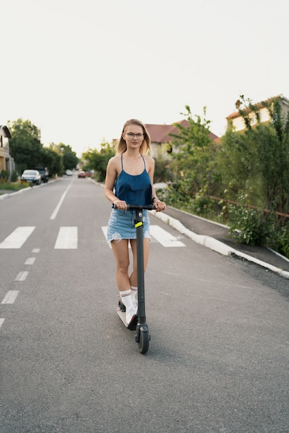 Menina bonita, montando uma scooter elétrica no verão na rua