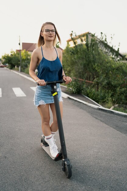 Menina bonita, montando uma scooter elétrica no verão na rua