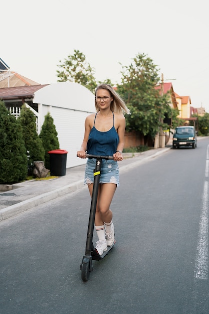 Menina bonita, montando uma scooter elétrica no verão na rua