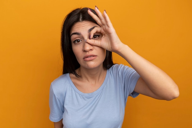 Foto grátis menina bonita morena caucasiana confiante olhando para a câmera através dos dedos em laranja