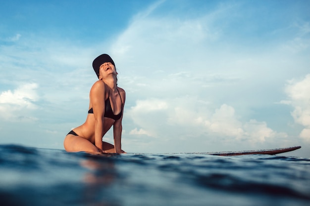 Menina bonita posando sentado em uma prancha de surf no oceano