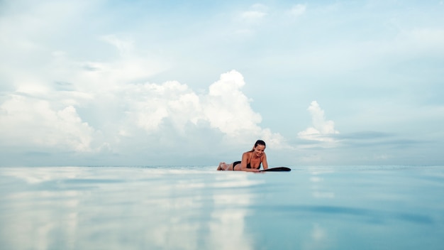 Menina bonita posando sentado em uma prancha de surf no oceano