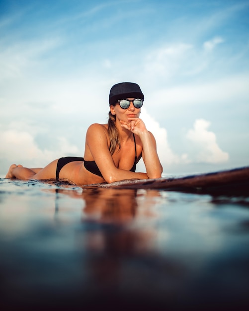 Menina bonita posando sentado em uma prancha de surf no oceano