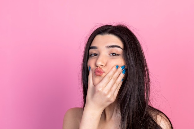 Menina bonita segurando a mão no rosto e de pé no fundo rosa foto de alta qualidade