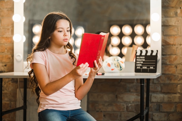 Foto grátis menina bonita sentada na frente do livro de leitura do espelho
