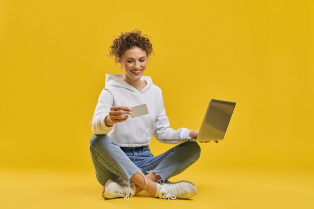 Menina bonita sentada nas pernas segurando o cartão e o laptop