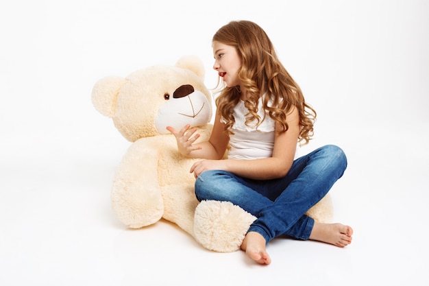 Menina bonita sentada no chão com urso de brinquedo, contando a história.