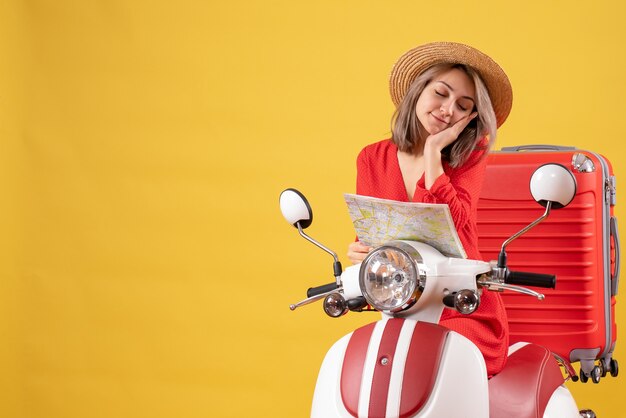 menina bonita sonolenta em ciclomotor com mala vermelha segurando mapa