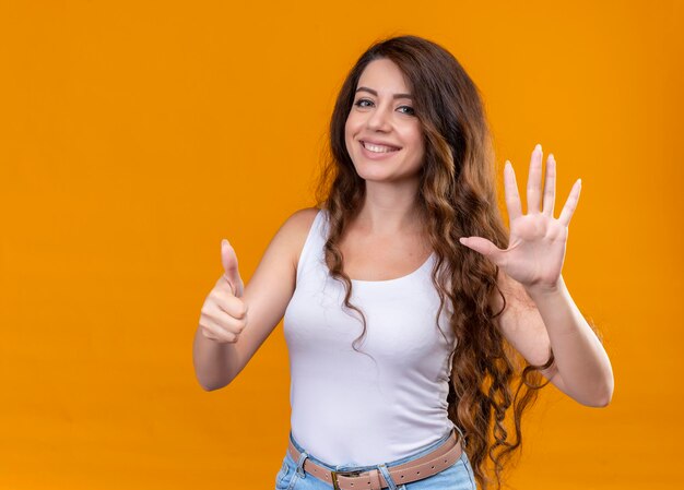 Menina bonita sorridente mostrando cinco e polegar para cima em um espaço isolado laranja com espaço de cópia