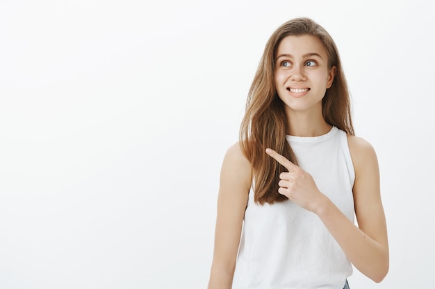 Menina bonita sorrindo e apontando para o canto esquerdo superior