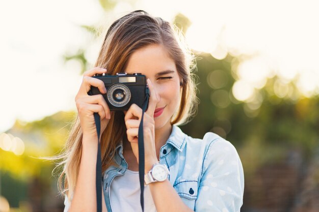 Menina bonita tirando fotos com uma câmera vintage em um dia ensolarado