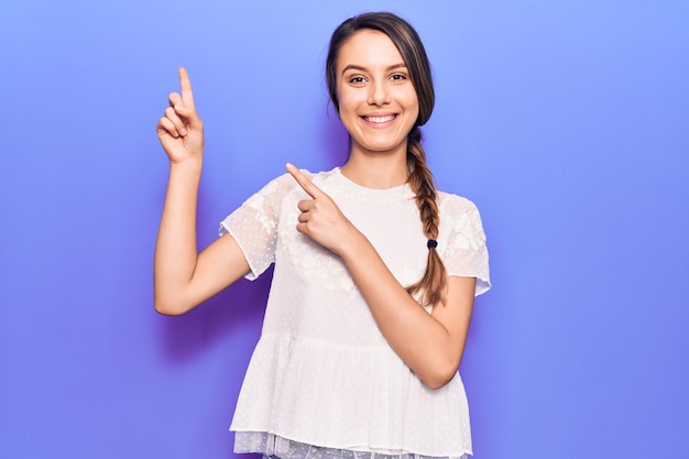 Menina bonita vestindo camiseta casual sorrindo e olhando para a câmera apontando com as duas mãos e os dedos para o lado.