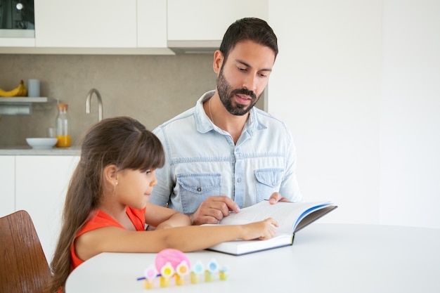 Menina bonitinha apontando para o texto e aprendendo com o pai.