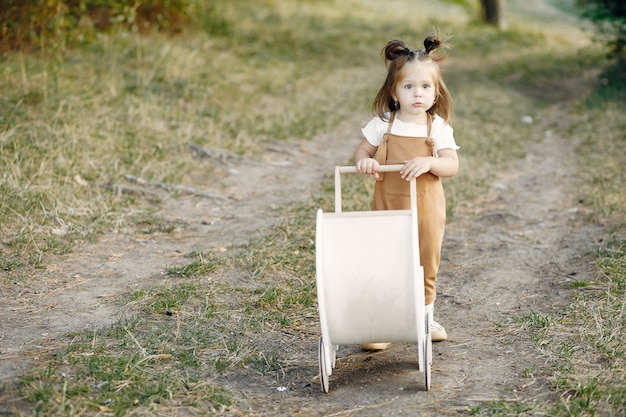 Menina bonitinha brincando em um parque com carruagem branca