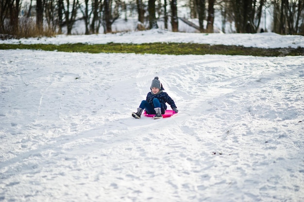 Menina bonitinha com trenós pires ao ar livre em dia de inverno