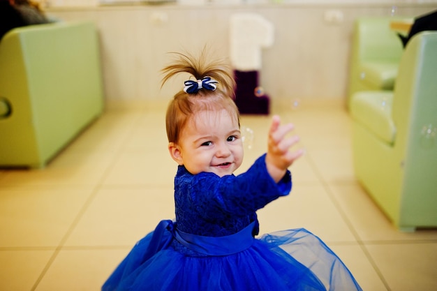 Menina bonitinha de vestido azul brincar com bolhas de sabão dia de aniversário de 1 ano