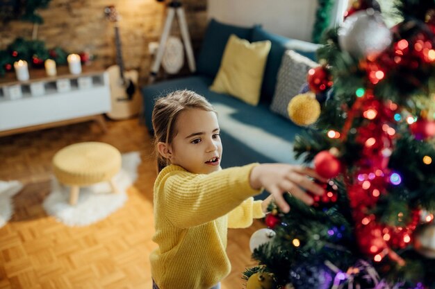 Menina bonitinha decorando a árvore de natal em casa