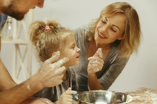 Menina bonitinha e seus lindos pais preparando a massa para o bolo na cozinha de casa