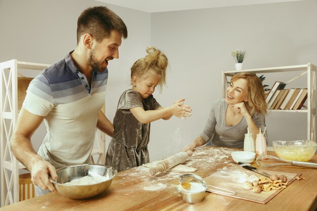 Menina bonitinha e seus lindos pais preparando a massa para o bolo na cozinha em casa. Conceito de estilo de vida familiar