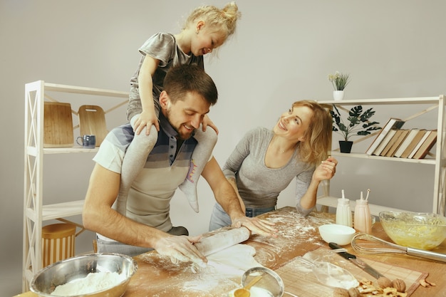 Menina bonitinha e seus lindos pais preparando a massa para o bolo na cozinha em casa. conceito de estilo de vida familiar