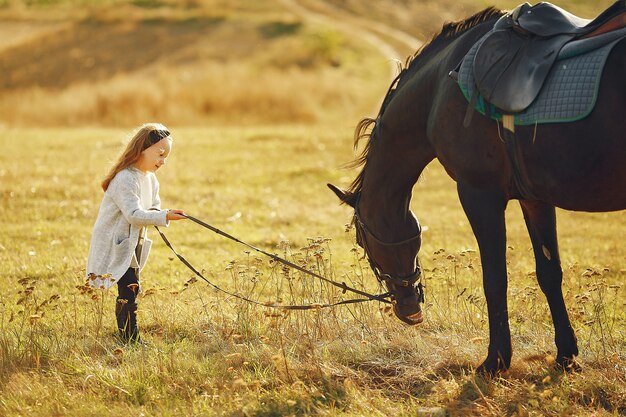 Menina bonitinha em um campo de outono com cavalo