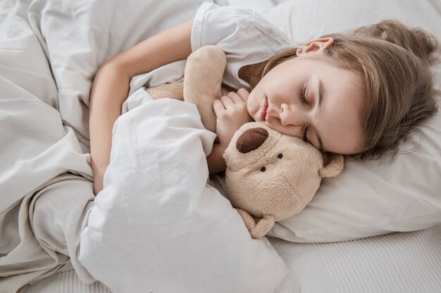 Menina bonitinha na cama com um brinquedo macio.