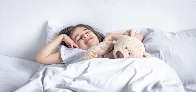 Menina bonitinha na cama com um ursinho de pelúcia no início da manhã