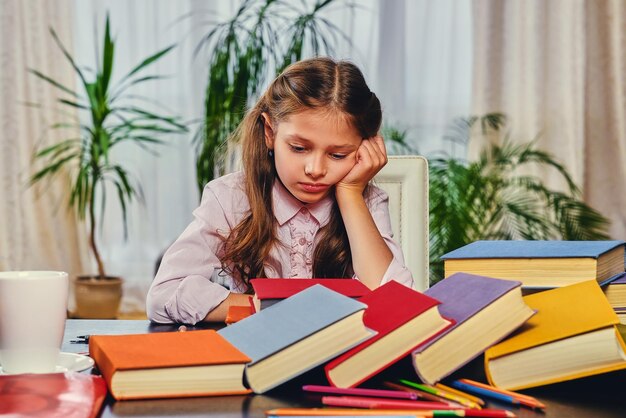 Menina bonitinha na mesa com um monte de livros coloridos.