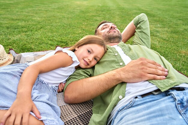 Menina bonitinha passando um tempo junto com seu pai relaxando deitado em um cobertor no