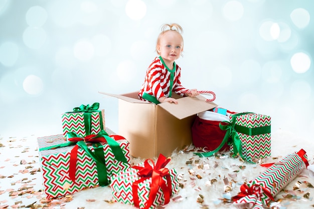 Menina bonito sentado na caixa sobre fundo de Natal. Feriado, celebração, conceito de criança