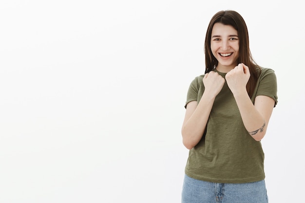 Foto grátis menina brincalhona se divertindo e fingindo estar lutando, convidando para lutar boxe segurando o punho cerrado em pose de boxeador defensivo perto da cabeça sorrindo e rindo brincando sobre a parede cinza