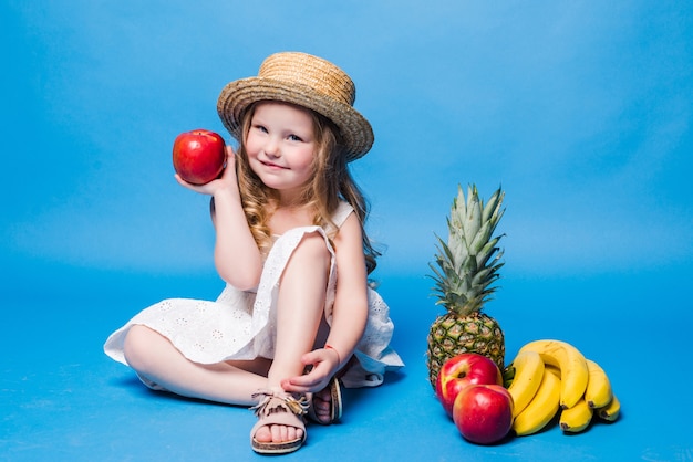 Menina brincando com frutas isoladas em uma parede azul