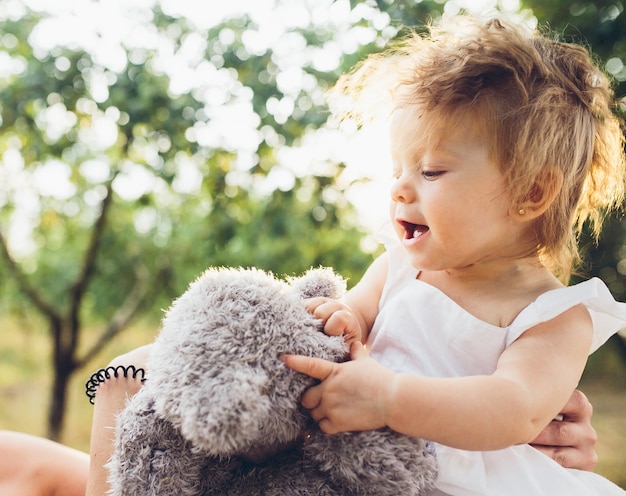 Menina brincando com um ursinho de pelúcia no jardim