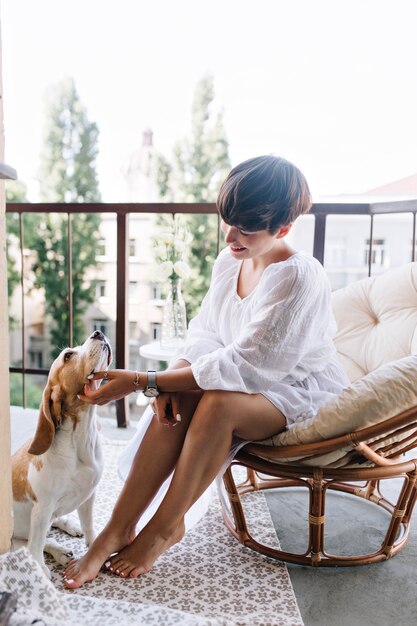 Menina bronzeada com manicure elegante e pedicure brincando com cachorro beagle engraçado que descansa no tapete