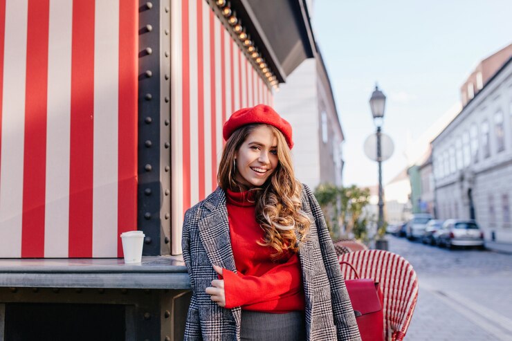 Foto grátis menina cacheada de cabelos castanhos com sorriso sincero, posando com um casaco cinza em uma bela rua europeia