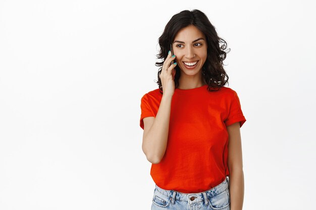 Menina cândida sorridente falando no telefone, conversa feliz, bate-papo com alguém, ligando no smartphone, usando roupas casuais em branco