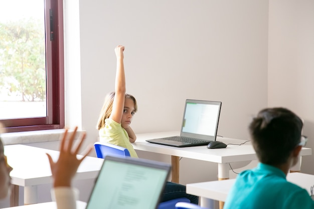 Menina caucasiana levantando a mão para responder durante a aula