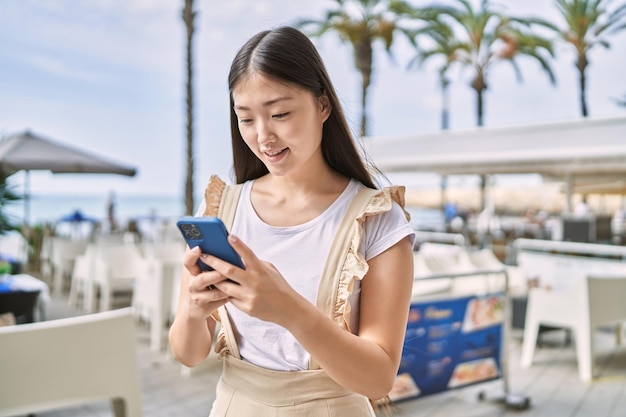 Menina chinesa sorrindo feliz usando smartphone no passeio