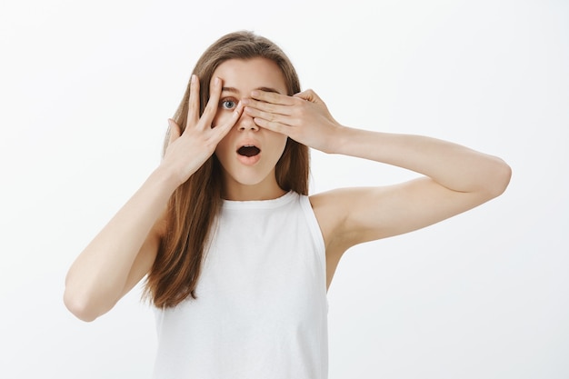 Menina chocada e emocionada cobrindo os olhos com as mãos, mas espiando por entre os dedos, curiosa para saber o que está acontecendo