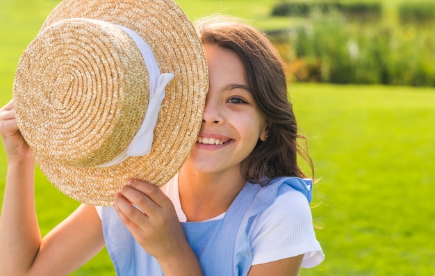 Menina, cobrindo o olho com um chapéu