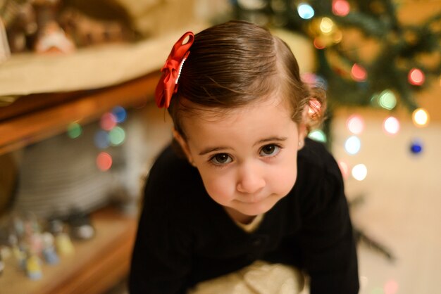 menina com arco no cabelo em casa com decoração e luzes de Natal desfocadas.