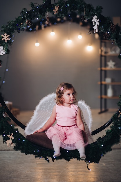 Menina com asas de anjo sentado na coroa do abeto.