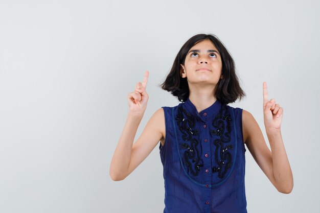 Menina com blusa azul apontando o dedo para cima e parecendo agradecida