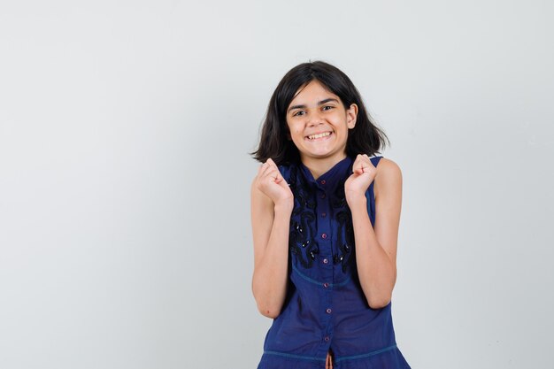 Menina com blusa azul mostrando gesto de vencedor e parecendo feliz