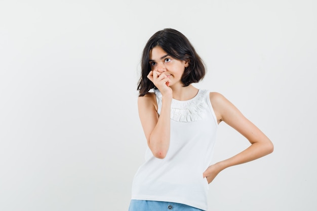 Menina com blusa branca, shorts olhando para longe e olhando pensativa, vista frontal.