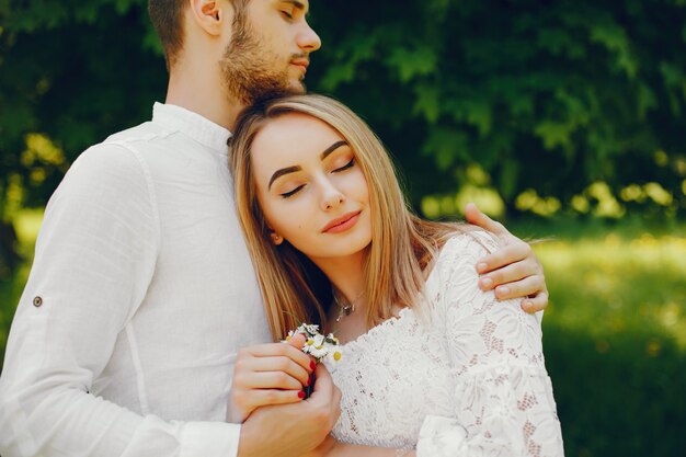 menina com cabelo claro e um vestido branco em uma floresta ensolarada com o namorado