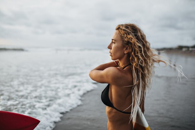 Menina com cabelo loiro ondulado olhando para o mar