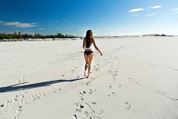 Menina com cabelos longos anda na praia branca