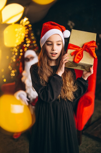 Menina com caixa de presente e santa no fundo sentado no sofá